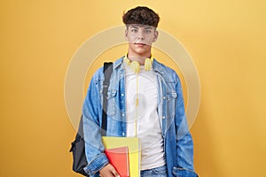 Hispanic teenager wearing student backpack and holding books relaxed with serious expression on face