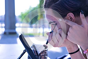 Hispanic transgender young adult girl painting her eyes with eyeliner in front of a hand mirror. Concept of transsexuality,