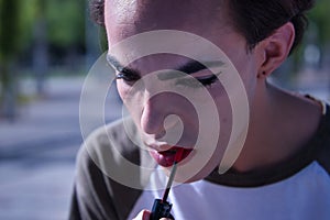 Hispanic and transsexual young adult girl painting her lips in front of a hand mirror. Concept of transsexuality, inclusion and