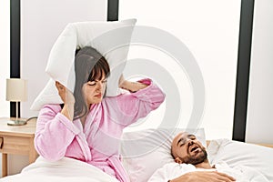 Hispanic woman angry with pillow on his ears while man snoring on the bed