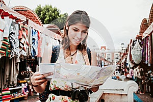 Hispanic woman backpacker holding a map and camera in a traditional mexican Market in Mexico, Vacations