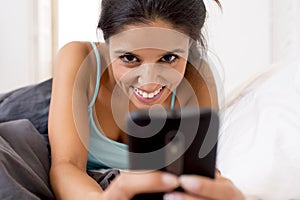 Hispanic woman in bed texting internet surfing on mobile phone in social network addiction