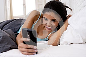 Hispanic woman in bed texting internet surfing on mobile phone in social network addiction