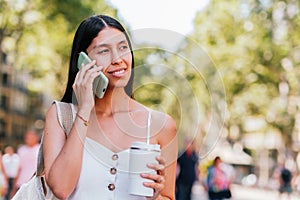 Hispanic woman with coffee speaking on smartphone