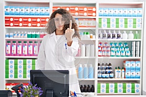 Hispanic woman with curly hair working at pharmacy drugstore showing middle finger, impolite and rude fuck off expression