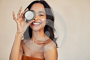 Hispanic woman holding beauty cream jar while smiling