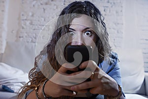 Hispanic woman holding mobile phone in crazy eyes social network and internet addiction concept