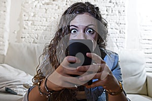 Hispanic woman holding mobile phone in crazy eyes social network and internet addiction concept