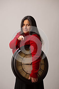 Hispanic Woman Holds Clock Under Arm And Points To Camera