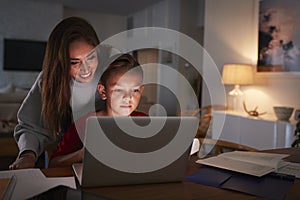 Hispanic woman looking over her sonï¿½s shoulder while he does his homework using laptop computer