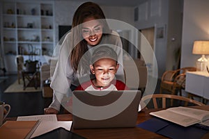 Hispanic woman looking over her sonï¿½s shoulder while he does his homework using laptop computer