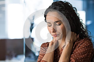 Hispanic woman overtired working in modern office businesswoman has severe neck pain, massages neck muscles, business photo
