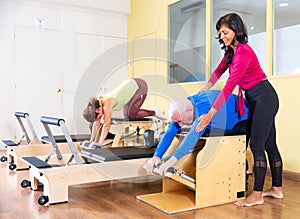 Hispanic woman pilates instructor helping senior man exercising on combo chair