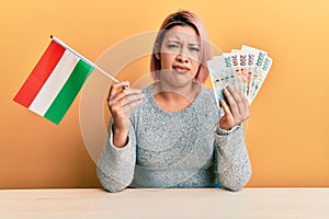 Hispanic woman with pink hair holding czech republic flag and koruna banknotes clueless and confused expression