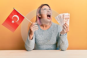 Hispanic woman with pink hair holding turkey flag and liras banknotes angry and mad screaming frustrated and furious, shouting