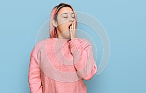 Hispanic woman with pink hair wearing casual winter sweater bored yawning tired covering mouth with hand