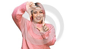 Hispanic woman with pink hair wearing casual winter sweater smiling making frame with hands and fingers with happy face