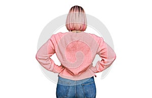 Hispanic woman with pink hair wearing casual winter sweater standing backwards looking away with arms on body