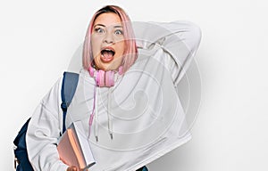 Hispanic woman with pink hair wearing student backpack and headphones crazy and scared with hands on head, afraid and surprised of