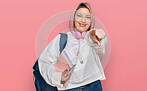 Hispanic woman with pink hair wearing student backpack and headphones pointing to you and the camera with fingers, smiling