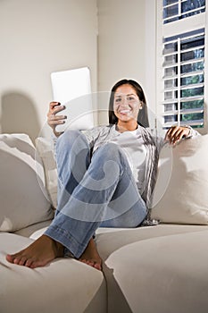 Hispanic woman reading electronic book on couch