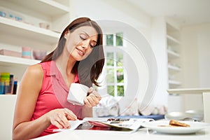 Hispanic Woman Reading Magazine In Kitchen