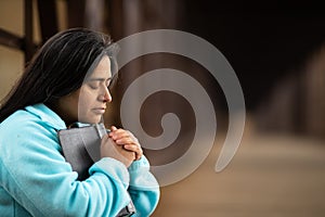 Hispanic Woman Sitting On A Bridge Praying While Holding Bible