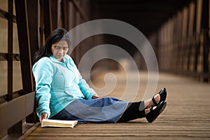 Hispanic Woman Sitting And Reading Bible On A Bridge