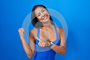 Hispanic woman standing over blue background pointing to the back behind with hand and thumbs up, smiling confident