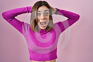 Hispanic woman standing over pink background crazy and scared with hands on head, afraid and surprised of shock with open mouth