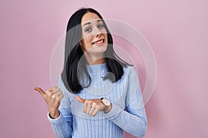 Hispanic woman standing over pink background pointing to the back behind with hand and thumbs up, smiling confident