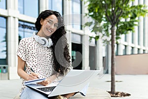 Hispanic woman student studying outdoors with laptop