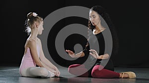 Hispanic woman teacher coach trainer talking to little girl student ballerina gymnast teenager dancer sitting on floor