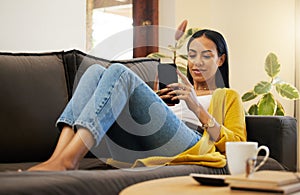 Hispanic woman using her smartphone while comfortable and relaxing in a bright living room. A young female lying on a