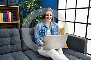 Hispanic woman using laptop at home looking positive and happy standing and smiling with a confident smile showing teeth