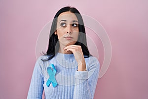 Hispanic woman wearing blue ribbon serious face thinking about question with hand on chin, thoughtful about confusing idea