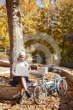 Hispanic woman working with her laptop outdoors. She is sitting next to a bicycle for a ride