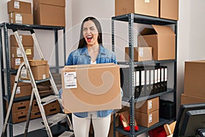 Hispanic woman working at small business ecommerce holding box angry and mad screaming frustrated and furious, shouting with anger