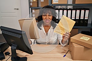 Hispanic woman working at small business ecommerce holding packages clueless and confused expression