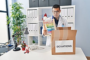 Hispanic young doctor man donating toys at the clinic skeptic and nervous, frowning upset because of problem