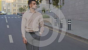 Hispanic young guy Arabian businessman walking near modern city building background. Confident adult bearded man walks