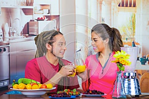 Hispanic young healthy couple enjoying breakfast together, sharing fruits, drinking orange juice and smiling, home
