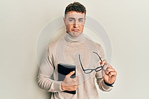 Hispanic young man reading a book and holding glasses depressed and worry for distress, crying angry and afraid