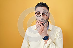 Hispanic young man wearing business clothes and glasses looking fascinated with disbelief, surprise and amazed expression with