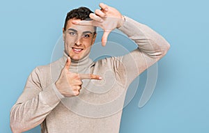 Hispanic young man wearing casual turtleneck sweater smiling making frame with hands and fingers with happy face
