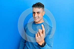 Hispanic young man wearing casual winter sweater beckoning come here gesture with hand inviting welcoming happy and smiling