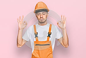 Hispanic young man wearing handyman uniform and safety hardhat relax and smiling with eyes closed doing meditation gesture with