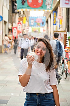 Hispanic young woman eating nikuman at Dotonbori street in Osaka, Japan.