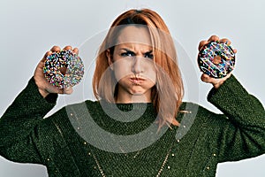 Hispanic young woman holding tasty colorful doughnuts puffing cheeks with funny face