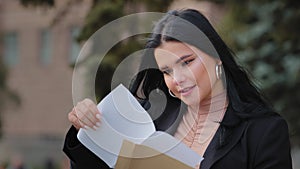 Hispanic young woman sitting on street opens paper letter read good news beautiful girl happy smiling female got dream